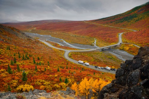 A winding road through vibrant autumn foliage, with RVs parked along the roadside in a mountainous landscape.