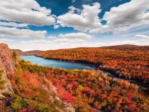 A vibrant autumn landscape featuring colorful trees, a serene lake, and a blue sky with fluffy clouds.