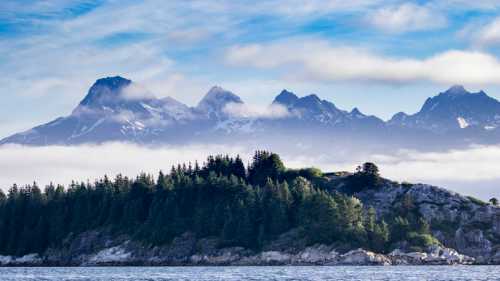 A serene landscape featuring a forested island in the foreground and majestic mountains shrouded in clouds in the background.