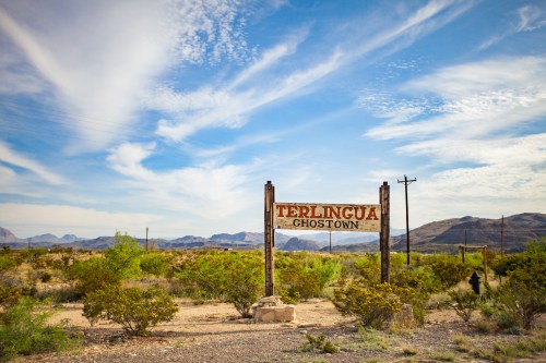 Sign for Terlingua Ghostown in a desert landscape with mountains and a blue sky.