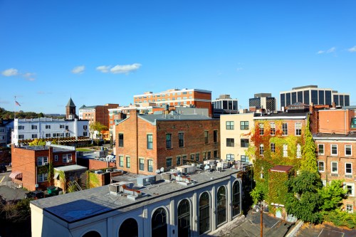 A cityscape featuring a mix of brick buildings, greenery, and modern structures under a clear blue sky.