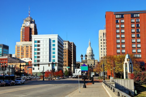 Cityscape featuring modern buildings, a historic dome, and clear blue skies, with trees showing autumn colors.
