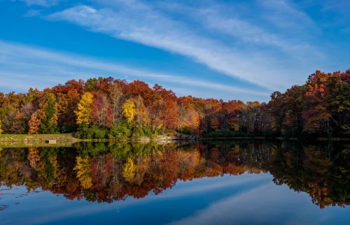 A serene lake reflecting vibrant autumn foliage under a clear blue sky.