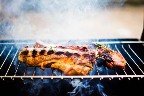 Grilled meat sizzling on a barbecue grill, surrounded by smoke and garnished with herbs.