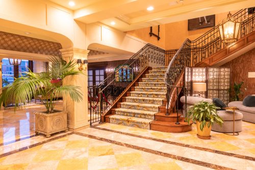 Elegant hotel lobby featuring a grand staircase, decorative plants, and stylish seating areas with warm lighting.