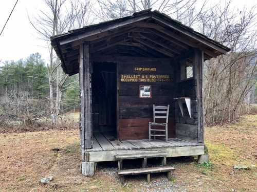 A small, rustic post office building with a sign reading "Smallest U.S. Post Office" and a single chair on the porch.