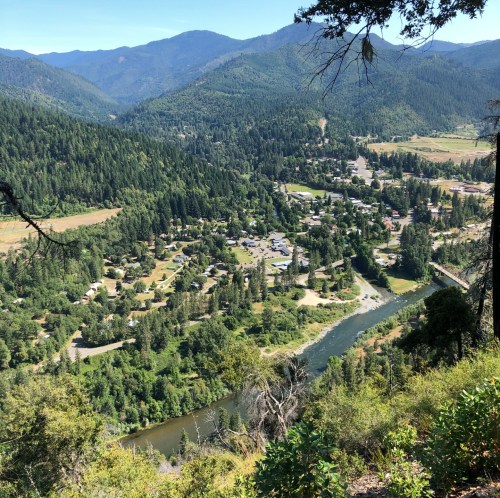Aerial view of a lush valley with a river, surrounded by mountains and a small town nestled among trees.