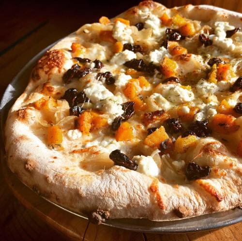 A freshly baked pizza topped with butternut squash, goat cheese, and dried fruit on a golden crust.