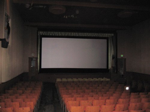 Empty movie theater with rows of orange seats facing a large, blank screen.