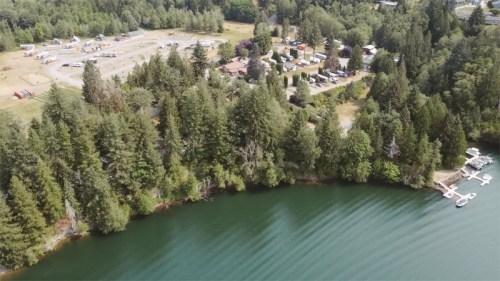 Aerial view of a serene lake surrounded by trees, with a campsite and boats docked along the shore.