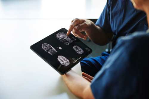 A medical professional examines brain scans on a tablet while discussing with a patient.