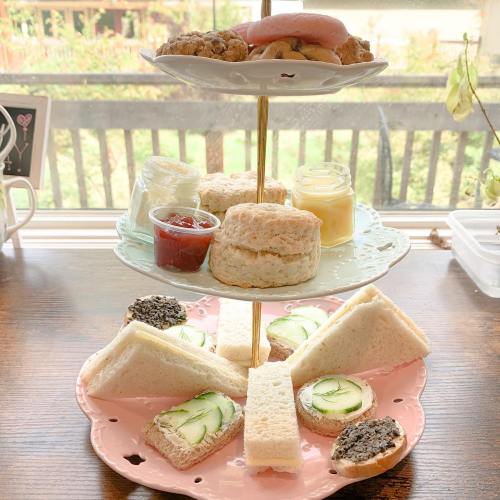 A tiered stand with assorted treats: cookies, scones, jam, mini sandwiches, and desserts, set by a window.
