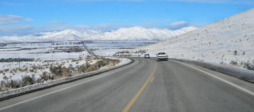 A winding road through a snowy landscape with mountains in the background and vehicles driving along the highway.
