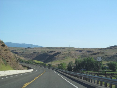 A winding highway stretches through a hilly landscape under a clear blue sky, with a road sign indicating Highway 95.
