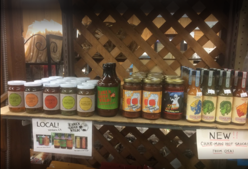 A shelf displaying various jars of hot sauces and condiments, labeled with colorful designs and local branding.