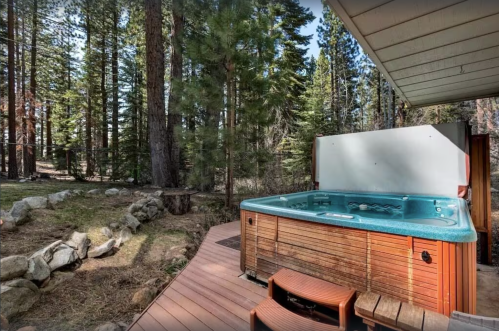 A wooden hot tub on a deck surrounded by tall trees and a natural landscape.