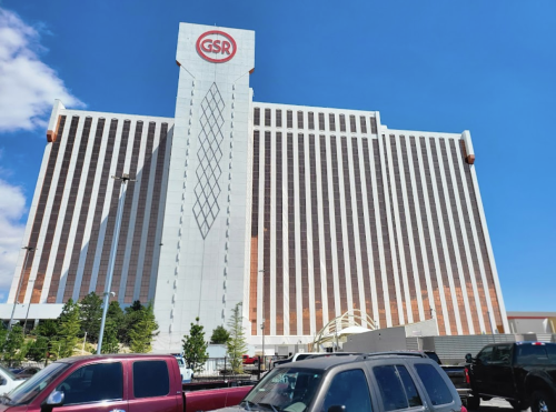 A tall hotel and casino building with a diamond pattern, under a clear blue sky, surrounded by parked cars.