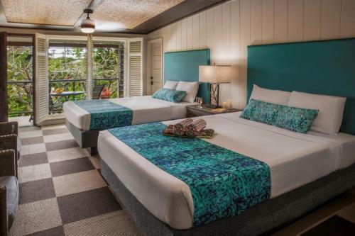 A cozy hotel room with two beds, tropical decor, and a balcony overlooking lush greenery.