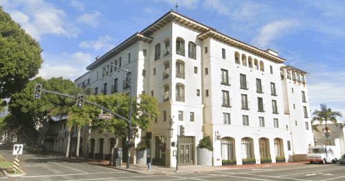 A white, multi-story building with a Spanish-style design, located at a street intersection under a blue sky.