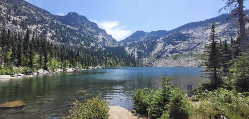 A serene lake surrounded by mountains and lush greenery under a clear blue sky.