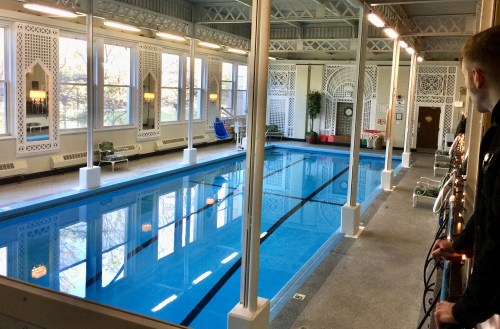 Indoor swimming pool with clear blue water, surrounded by elegant architecture and large windows letting in natural light.