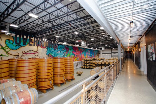 Interior of a winery featuring wooden barrels and colorful murals on the walls, with a spacious corridor.
