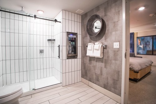 Modern bathroom featuring a glass shower, towel rack, and a mirror, with a view of a bedroom in the background.