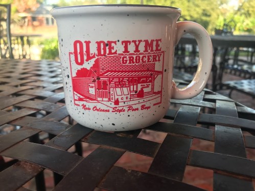 A speckled mug featuring "Olde Tyme Grocery" and an illustration of a building, resting on a metal table.