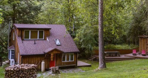 A cozy cabin surrounded by lush green trees, with a separate deck area and outdoor seating.