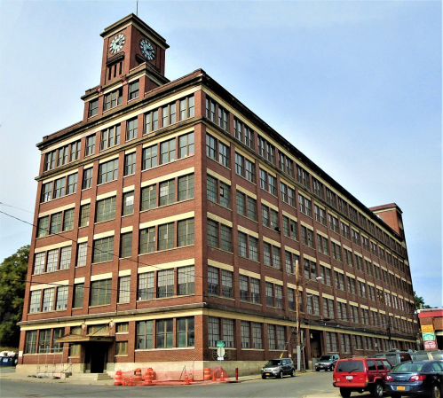 Historic brick building with a clock tower, featuring large windows and a prominent entrance, set against a clear sky.