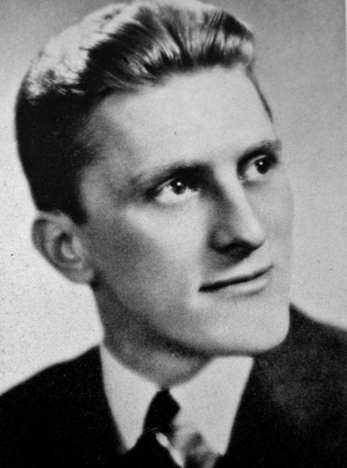 Black and white portrait of a young man with slicked-back hair, wearing a suit and tie, looking thoughtfully to the side.