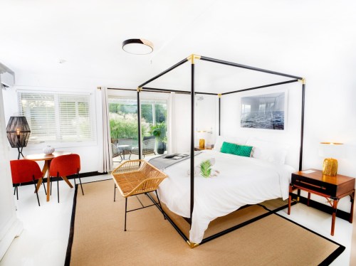 Bright, modern bedroom with a four-poster bed, stylish furniture, and large windows overlooking greenery.