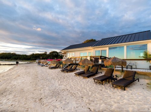 A beachside scene featuring lounge chairs, thatched umbrellas, and a modern building under a cloudy sky.