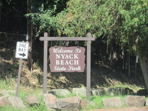 A wooden sign welcoming visitors to Nyack Beach State Park, with a one-way traffic sign nearby.
