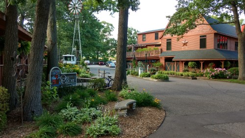 A scenic view of a charming lodge surrounded by greenery, flowers, and a windmill in the background.