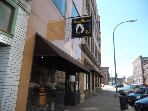 Exterior view of Valley Monster Pub, featuring a sign and a street lined with parked cars and buildings.
