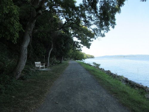 A peaceful path along a river, lined with trees, featuring a bench overlooking the water.