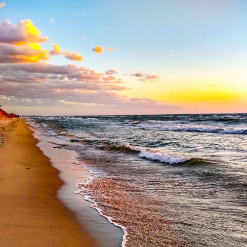 A serene beach at sunset, with gentle waves lapping at the shore and colorful clouds in the sky.