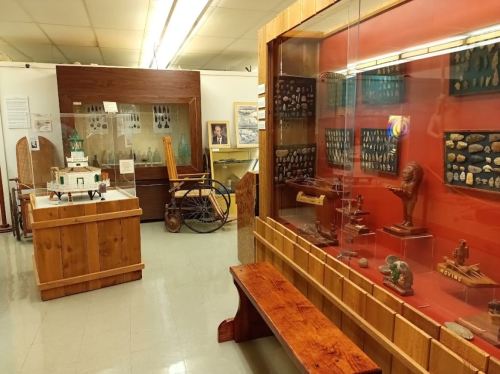 A museum interior featuring display cases with artifacts, wooden benches, and various historical items on exhibit.