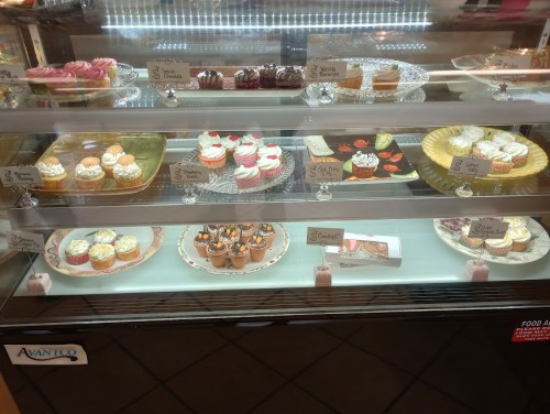 A display case filled with various colorful cupcakes and desserts, each labeled with prices.