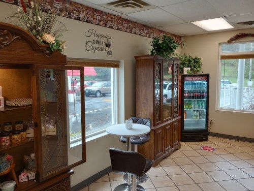 Cozy café interior with a display cabinet, small table, and a drink fridge, featuring a cheerful cupcake-themed wall.