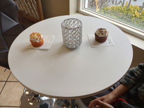 A round table with two cupcakes and a decorative candle holder in a bright cafe setting.