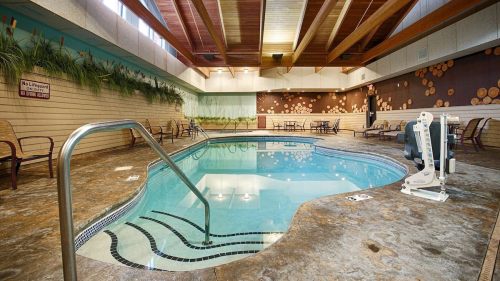Indoor swimming pool with a ramp, surrounded by lounge chairs and decorative wall art. Bright, spacious atmosphere.