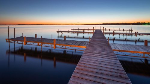 A serene lake at sunset, featuring wooden docks extending into calm waters, reflecting the colorful sky.