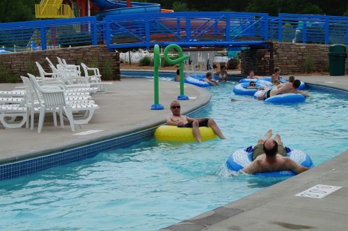 People relaxing on inflatable tubes in a lazy river pool, with lounge chairs and water slides in the background.