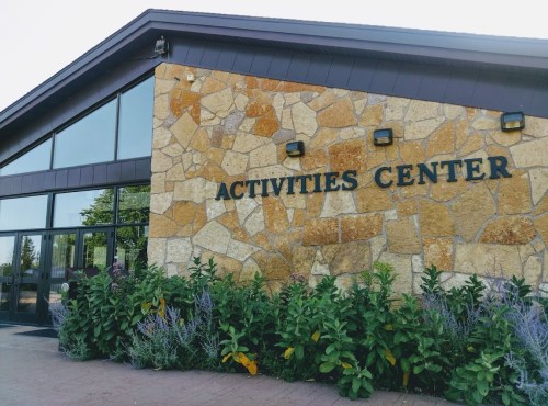Exterior of a building labeled "Activities Center," featuring a stone wall and surrounding greenery.