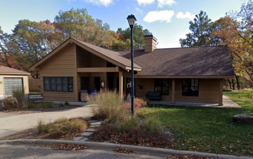 A brown wooden building with a sloped roof, surrounded by trees and autumn foliage, serving as a campground office.