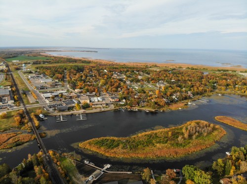 Aerial view of a small town surrounded by water and autumn-colored trees, with a calm lake and marshland nearby.
