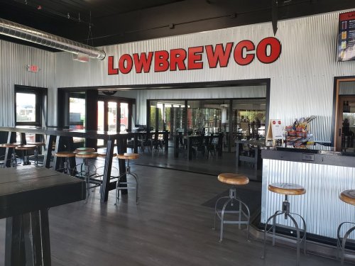 Interior of a brewery with metal walls, high tables, and a large glass window displaying the name "LOWBREWCO."