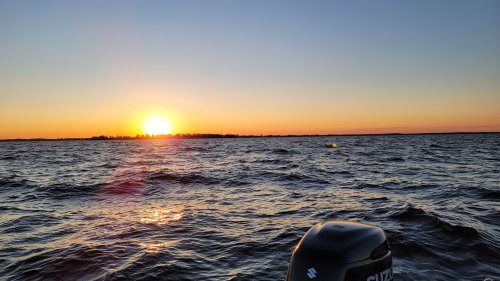 A serene sunset over a calm lake, with gentle waves and a silhouette of trees on the horizon.